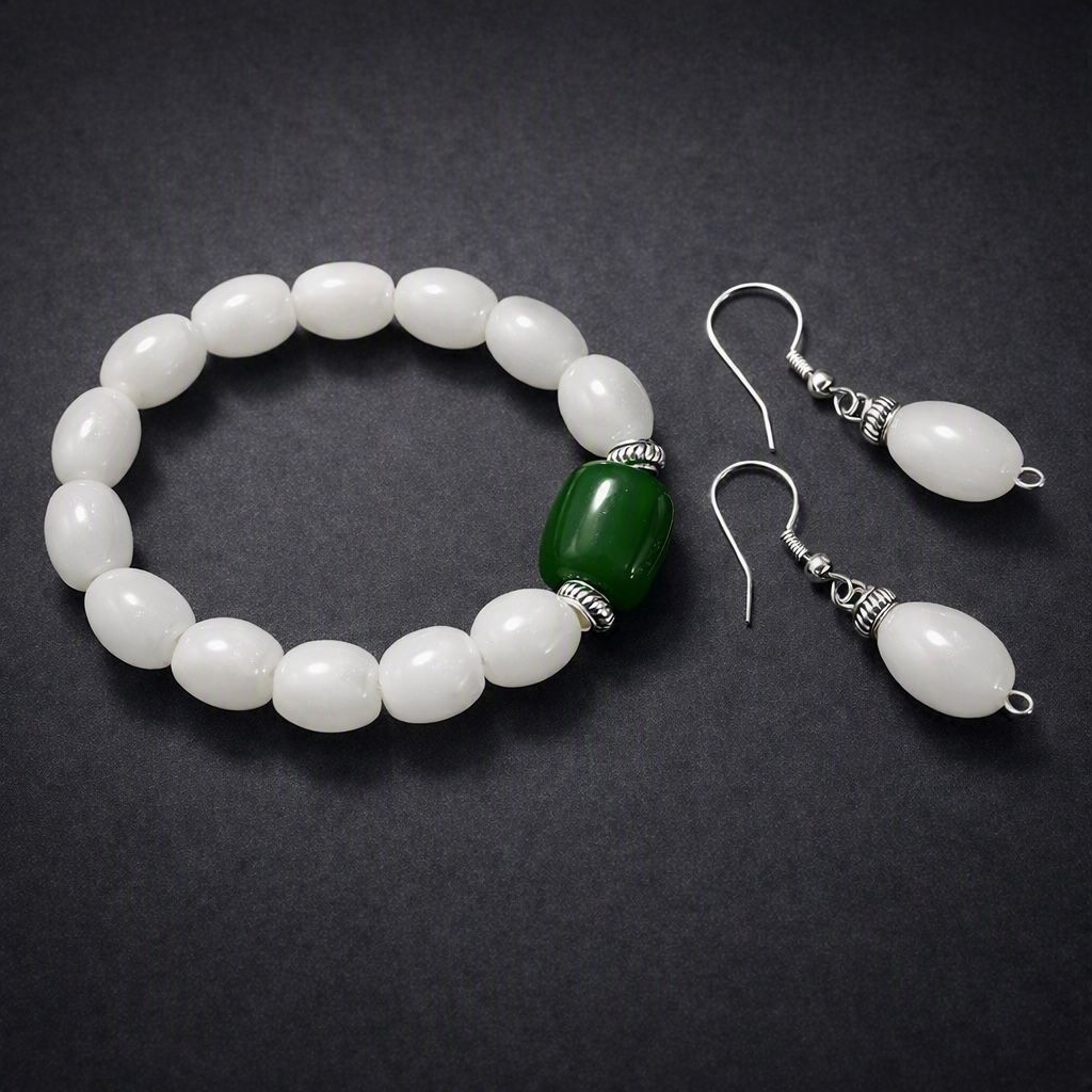 White jade bracelet with a single green jade bead, and matching white jade drop earrings, on dark slate